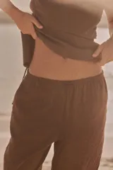 Pantalón marrón de tejido fluido, tiro medio, cintura elástica ajustable con cordones, bolsillos laterales y falsos bolsillos de vivo en la espalda.