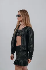 Campera bomber color beige de cuero, con cuello redondo, cierre frontal con botones a presión, mangas largas con puños elásticos y detalles de tachas metálicas en hombros y espalda.