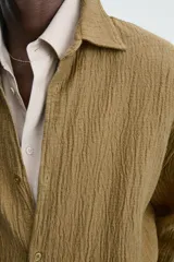 Sobrecamisa color caqui de algodón y lino con efecto arrugado, corte relaxed fit, cuello solapa, manga larga con puños abotonados y cierre frontal con botones.