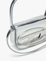 Bolso Diesel modelo 1DR, color negro charolado, con asa corta superior y correa bandolera extraíble. Presenta solapa con cierre magnético y logo ovalado "D" metálico en el frente.
