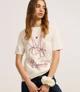 Remera color crudo de algodón, con cuello redondo y mangas cortas. Estampa frontal con dibujo de zapatillas de ballet, corazón y texto "La Coquette avec tout mon amour".