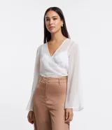 Blusa cropped de chiffon color blanco, con escote en V cruzado, mangas largas acampanadas y lazo en la espalda.