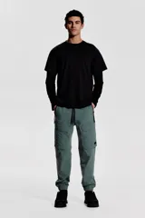 Pantalón jogger deportivo color verde grisáceo, con cintura elástica ajustable con cordón, bolsillos laterales con cierre, bolsillos cargo con solapa y bajos elásticos.