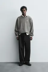 Sudadera gris con rayas verticales blancas, cuello redondo, manga larga y bordado con texto en el pecho.