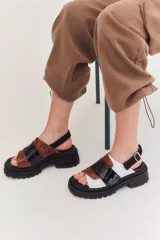 Sandalias marrones con tiras anchas de cuero texturizado y gamuza, suela track negra y hebilla ajustable en el tobillo.