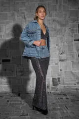 Falda larga de tiro alto, confeccionada en tela elástica cubierta de lentejuelas negras. Presenta una sección superior de denim con bolsillos y corte a la cadera.