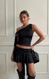 Top negro ajustado al cuerpo, de corte asimétrico con un solo hombro y tirante fino que se anuda en el hombro.