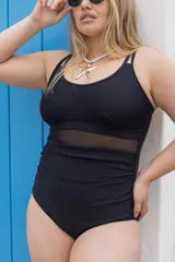 Traje de baño entero negro con breteles finos y espalda baja. Presenta una sección de malla transparente en la zona del abdomen y frunces laterales.