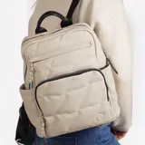 Mochila color beige con diseño acolchado en forma de rombos. Tiene un bolsillo frontal con cierre, dos bolsillos laterales abiertos y un bolsillo interno con cierre. Las correas son ajustables y tiene un asa superior para llevar en la mano.