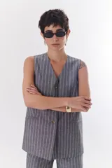 Chaleco gris con finas rayas verticales blancas, con cuello en V, cierre frontal con botones y bolsillos laterales.