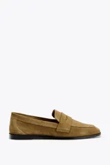 Zapato plano tipo mocasín color marrón claro, confeccionado en piel de serraje. Tiene copete subido, antifaz y acabado en punta redonda.
