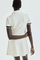Vestido corto blanco de piqué con cuello polo, tapeta de botones y falda acampanada.