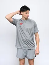 Remera deportiva gris con finas líneas horizontales y logo de Umbro en rojo en el pecho.