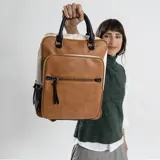 Mochila combinada en tres tonos de símil cuero: marrón, beige y negro. Tiene doble bolsillo frontal, asa de mano y correas regulables. En su interior tiene dos bolsillos con cierre y uno abierto con división para celular.