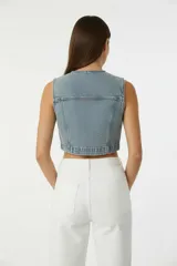 Chaleco corto de denim azul oscuro, estilo vaquero, con cuello en V, cierre frontal de botones y dos bolsillos de parche con tapa en el pecho.