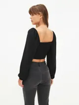 Blusa crop top negra con escote cuadrado, mangas largas abullonadas y lazo ajustable en el centro del busto.