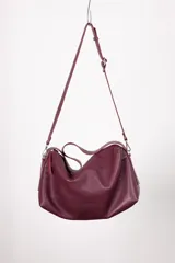 Bolso tipo hobo color borgoña, de cuero con textura granulada. Tiene correa de hombro ajustable y extraíble, cierre superior con cremallera, forro interior de algodón con bolsillo con cremallera y bolsillo abierto.