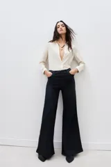 Pantalón de jean negro de tiro alto y pierna palazzo, confeccionado en denim con elastano y coating negro con apariencia similar al cuero.