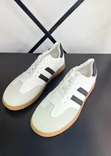 Championes blancos con detalles en negro, con tres tiras negras en el lateral y suela color caramelo.