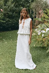Conjunto de top y falda color crema, confeccionado en lino. El top es sin mangas, con detalle de lazos en el escote y volados en el ruedo. La falda es larga y de corte recto.