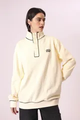 Buzo color crema con cuello alto con botones y ribete negro en cuello, puños y ruedo.
