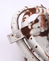 Cartera baguette de cuero con estampado animal print de vaca en tonos marrón y blanco. Tiene forro interior, un bolsillo amplio y broches laterales para ajustar el tamaño.