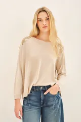 Sweater color beige con cuello redondo y mangas largas. Presenta apliques dorados en los hombros y un cinturón marrón con forma de flor.