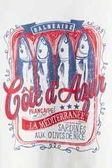Remera blanca de algodón con cuello redondo y mangas cortas. Estampado frontal con diseño de lata de sardinas con texto en francés y detalles en rojo y azul.
