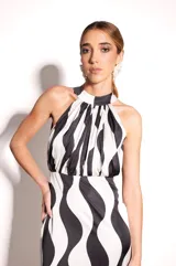 Vestido largo de seda estampada en blanco y negro con diseño geométrico ondulado. Tiene escote halter regulable, corte ajustado en busto y cintura, falda fluida con tajo delantero y tableado a mano en el frente.