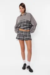 Minifalda gris con estampado de cuadros escoceses, cintura ancha, tablas en la parte inferior y cierre metálico lateral. Incluye sobrefalda desmontable con bolsillo.