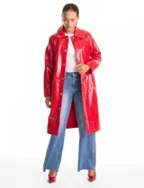 Chaqueta larga tipo trench de charol negro con acabado brillante e impermeable. Presenta cuello con solapa, cierre frontal con botones metálicos plateados y bolsillos laterales. Su diseño es de corte recto y estructura rígida.