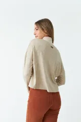 Cardigan tejido color beige con escote en V, cierre con botones, bolsillos delanteros y logo en grifa de cuero.