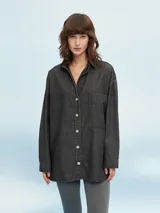Camisa de jean negra, de corte amplio, con cuello clásico, cierre frontal con botones y bolsillo de parche en el pecho.
