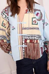 Camisa celeste con estampado de objetos y flores en tonos pastel, de manga larga y cuello en V con cierre de botones tipo alamar.