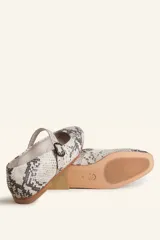 Zapato tipo Mary Jane de charol color borgoña, con punta redondeada, tira sobre el empeine con hebilla y suela de cuero.