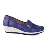 Zapato Korium color beige con capellada lisa, detalle de perforaciones y aplique metálico dorado. Tiene taco corrido blanco y suela marrón.