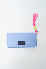 Billetera rectangular color fucsia con cierre perimetral y parche frontal negro con logo. Incluye correa de mano de cordón rosa neón y detalle de ajuste en verde lima.