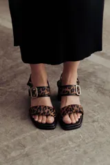 Sandalia de cuero color negro con taco bloque medio y punta cuadrada. Presenta dos tiras anchas sobre el empeine, una de ellas con hebilla metálica dorada, y una tira de sujeción en el talón. Posee base acolchonada para mayor comodidad.