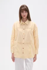 Camisa de algodón blanca, de corte ancho, con botones de madera y detalles de encaje calado en el frente, mangas y ruedo. Tiene cuello camisero y manga larga.