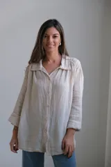 Camisa beige de lino, corte amplio, con cuello clásico, cierre frontal con botones y mangas largas con puños abotonados.