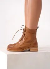Bota corta de cuero color marrón claro, con cordones y detalles de perforaciones. Tiene un pequeño taco de madera.