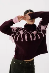 Sweater tejido de punto color crudo con cuello alto y diseño de rombos marrones con flecos.