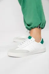 Zapatilla de cuero blanco con detalles en verde, diseñada para conjuntos casuales y estilo atemporal.