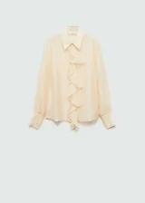 Camisa color crema de corte recto, con cuello camisero, cierre frontal con botones ocultos, manga larga con puños abotonados y detalle de volantes en el frente.