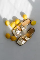 Sandalias bajas doradas con tiras entrelazadas y suela marrón.