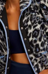 Chaqueta polar corta con cuello alto y cierre frontal de botones a presión. Presenta un estampado animal print en tonos azul marino, gris y blanco, con ribetes en color celeste.