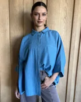 Camisa celeste de denim con cuello clásico, cierre frontal con botones y mangas 3/4.