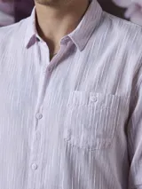 Camisa de manga larga color rosa con rayas verticales blancas, cuello clásico y bolsillo en el pecho. Cierre frontal con botones.