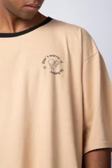 Remera color arena con manga corta negra, cuello redondo con ribete negro y estampado pequeño en el pecho con la frase "Don't worry be happy".