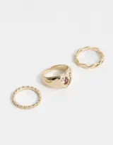 Set de tres anillos dorados de metal. Uno liso, otro con diseño de eslabones entrelazados y otro con forma de sello con una manzana esmaltada y strass.